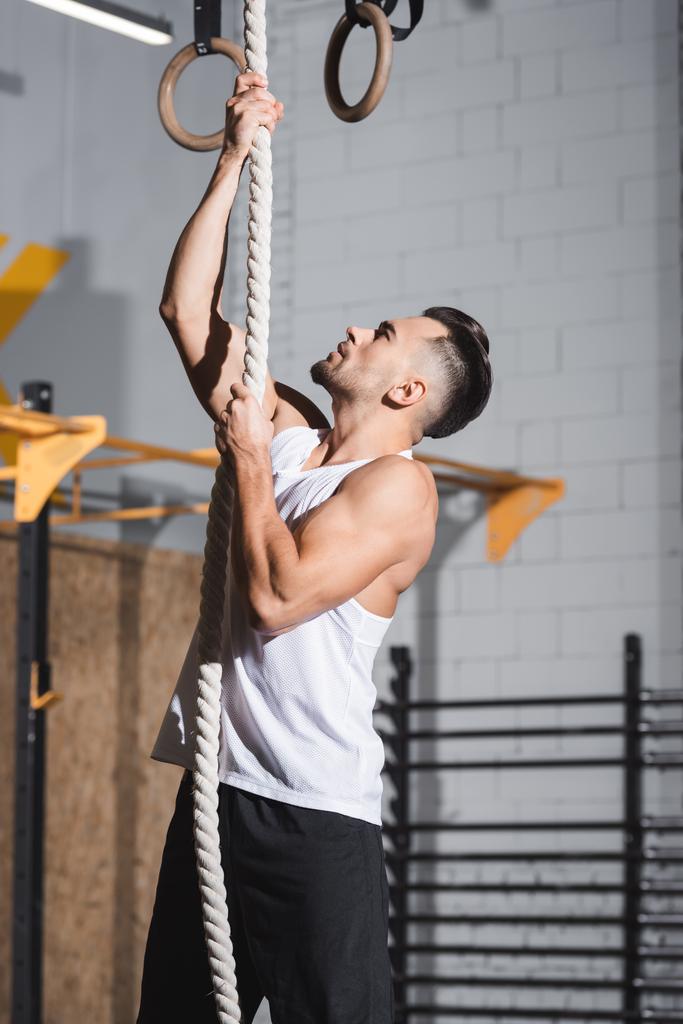 Oldalnézet atlétikai sportoló mászik kötélen tornaterem  - Fotó, kép