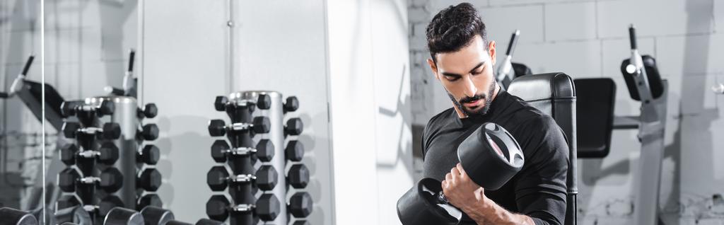 Bearded muslim sportsman training with dumbbell in gym, banner  - Photo, Image