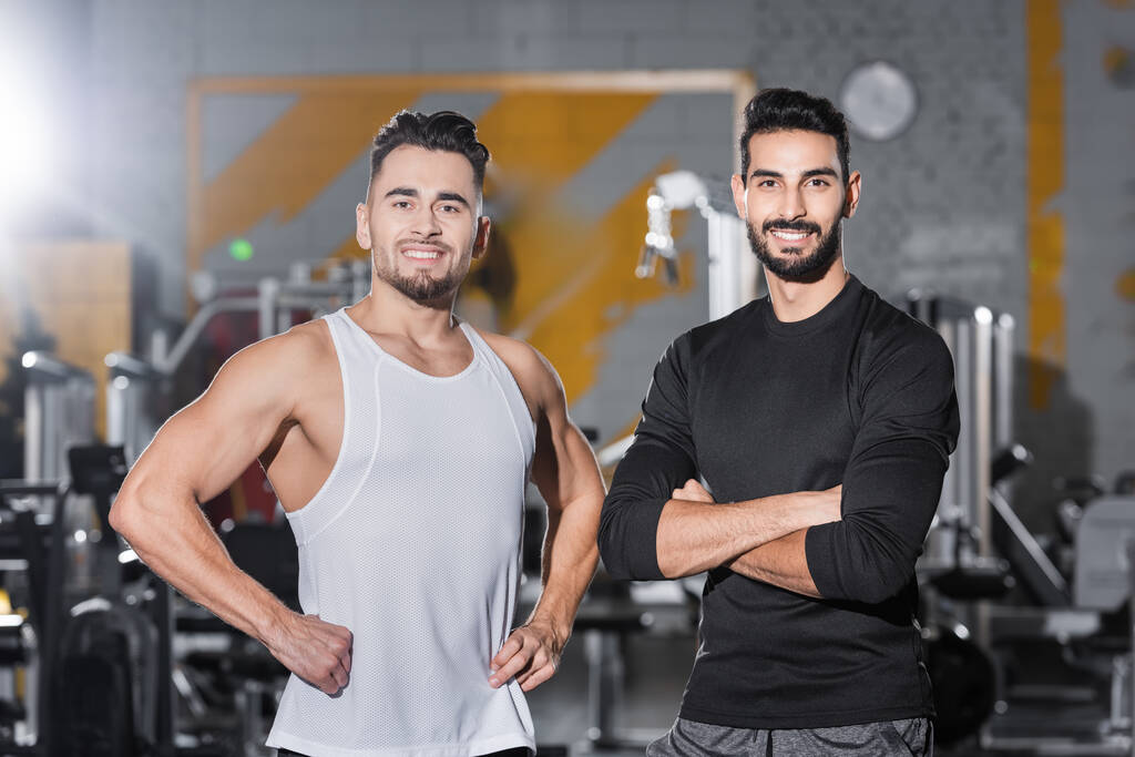 Smiling interracial sportsmen looking at camera in blurred gym  - Photo, Image