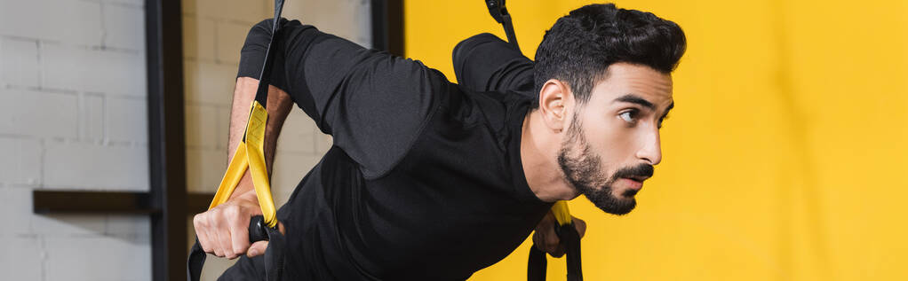 Молодой арабийский спортсмен дергает за ремни подвески в спорткомплексе, баннер  - Фото, изображение