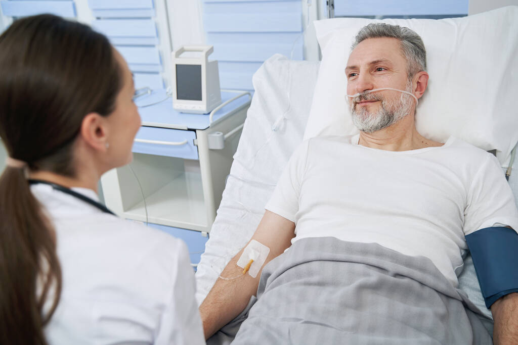 Mannelijke patiënt die communiceert met therapeut tijdens intraveneuze behandeling - Foto, afbeelding
