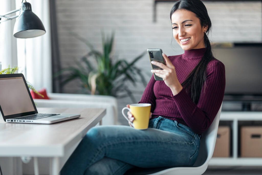 Foto de mujer de negocios enviando mensajes con su teléfono móvil mientras trabaja y bebe café en casa. - Foto, Imagen