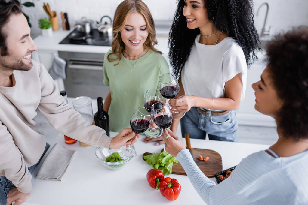 high angle view of happy multiethnic friends clinking glasses of red wine in kitchen  - Photo, Image