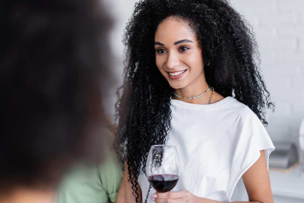 mujer afroamericana feliz sosteniendo copa de vino en la cocina  - Foto, imagen