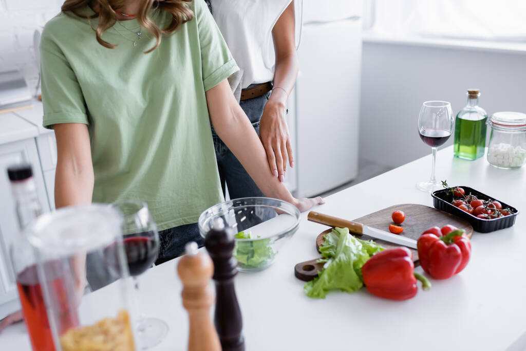 обрезанный вид молодых однополых пар, стоящих рядом с овощами на кухне - Фото, изображение