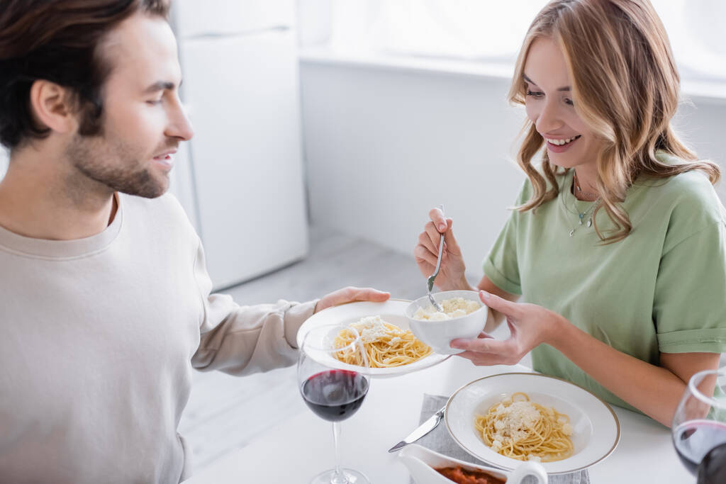 woman holding bowl with grated cheese near man holding plate with pasta - Photo, Image