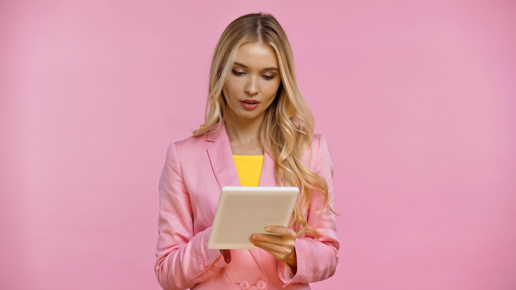 Femme blonde en veste utilisant une tablette numérique isolée sur rose  - Photo, image