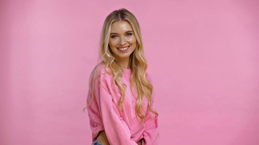 Happy blonde woman in sweatshirt looking at camera isolated on pink  - Photo, Image