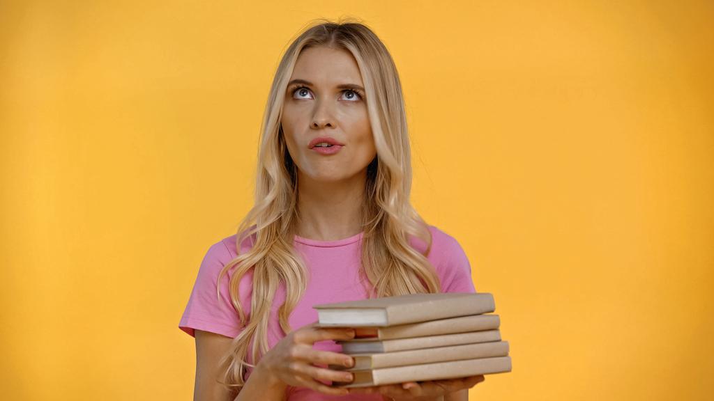 Skeptická blondýna drží knihy izolované na žluté  - Fotografie, Obrázek