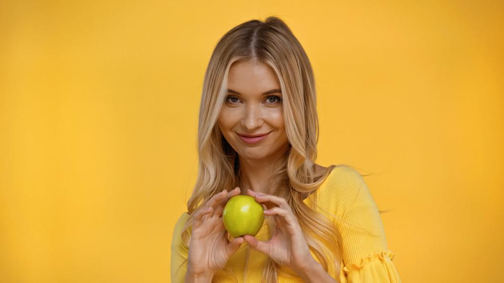 Femme blonde souriante tenant pomme fraîche isolée sur jaune  - Photo, image