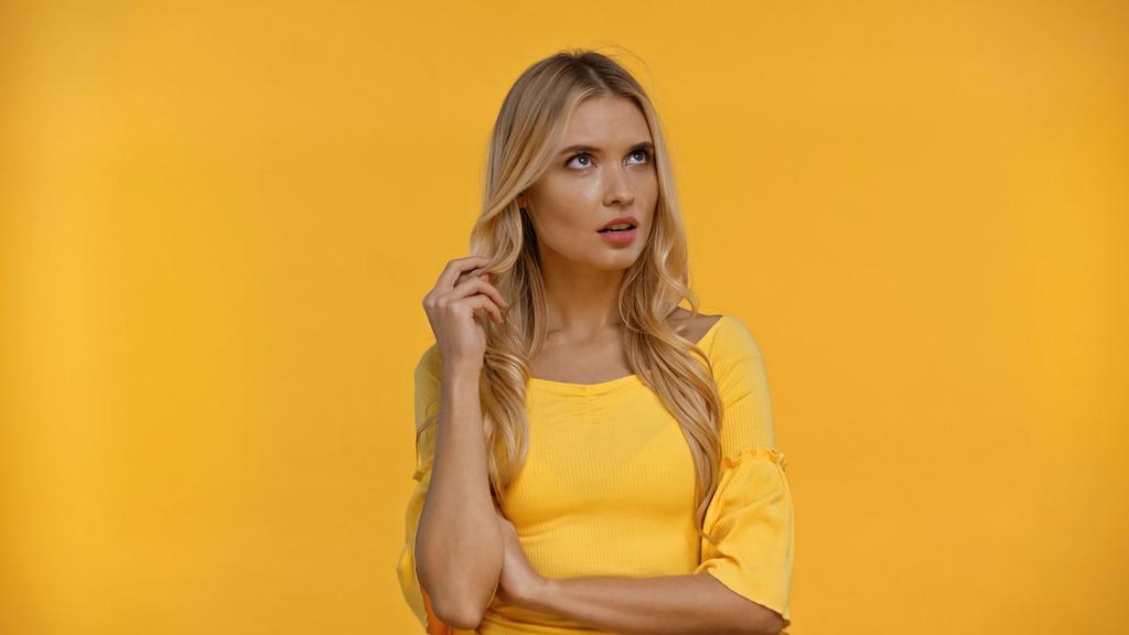 Pensiva donna bionda che tocca i capelli isolati sul giallo  - Foto, immagini