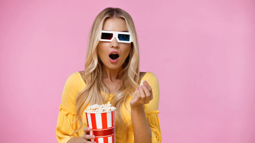 Femme blonde choquée dans des lunettes 3D tenant pop-corn isolé sur rose  - Photo, image
