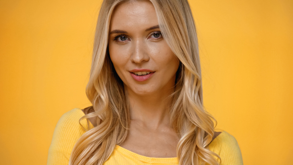 Красивая блондинка в блузке смотрит на камеру изолированной на желтый  - Фото, изображение
