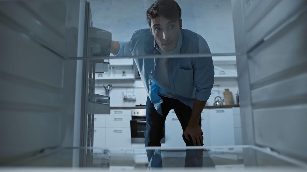 любопытный мужчина смотрит в пустой холодильник на кухне - Фото, изображение
