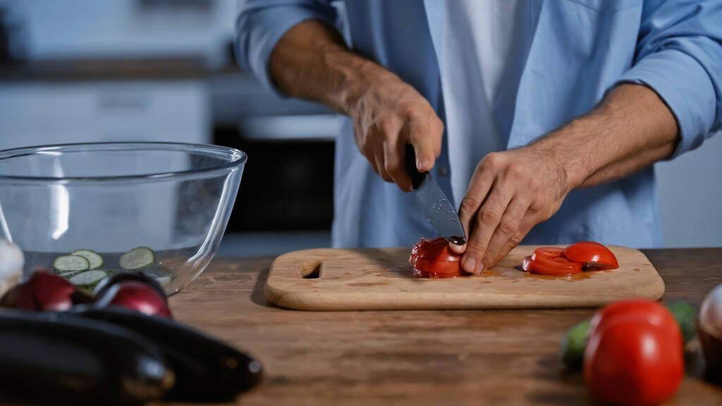 обрезанный вид человека, режущего спелые помидоры возле размытых баклажанов  - Фото, изображение