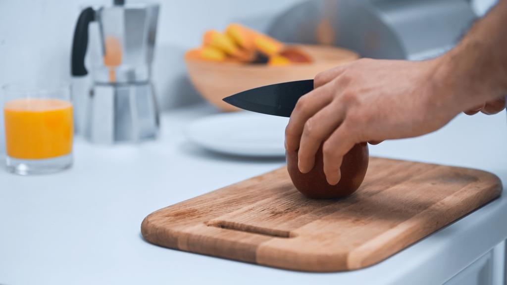visão parcial do homem cortando maçã madura em tábua de corte na cozinha - Foto, Imagem