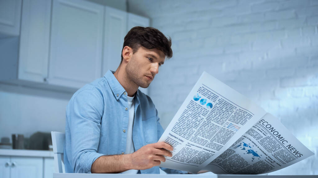 Mann im blauen Hemd liest Morgenzeitung, während er in der Küche sitzt - Foto, Bild
