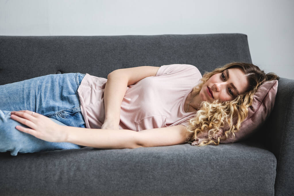 Nuori, surullinen nainen makaa sohvalla. Masentunut tyttö on kotona. Väsynyt nainen - Valokuva, kuva