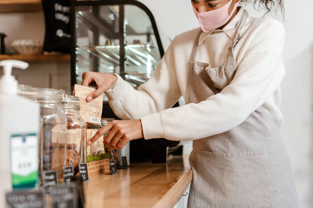 Black woman barista in face mask working at cafe counter indoors - Photo, Image