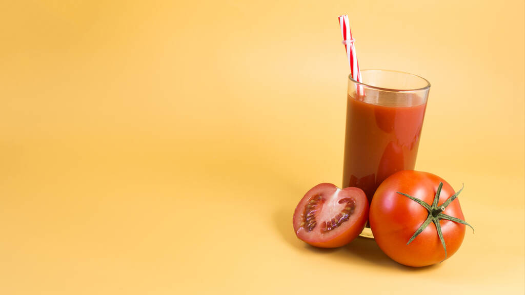 Suco de tomate com um tubo vermelho e tomates vermelhos em um fundo de espaço kopi amarelo brilhante. - Foto, Imagem