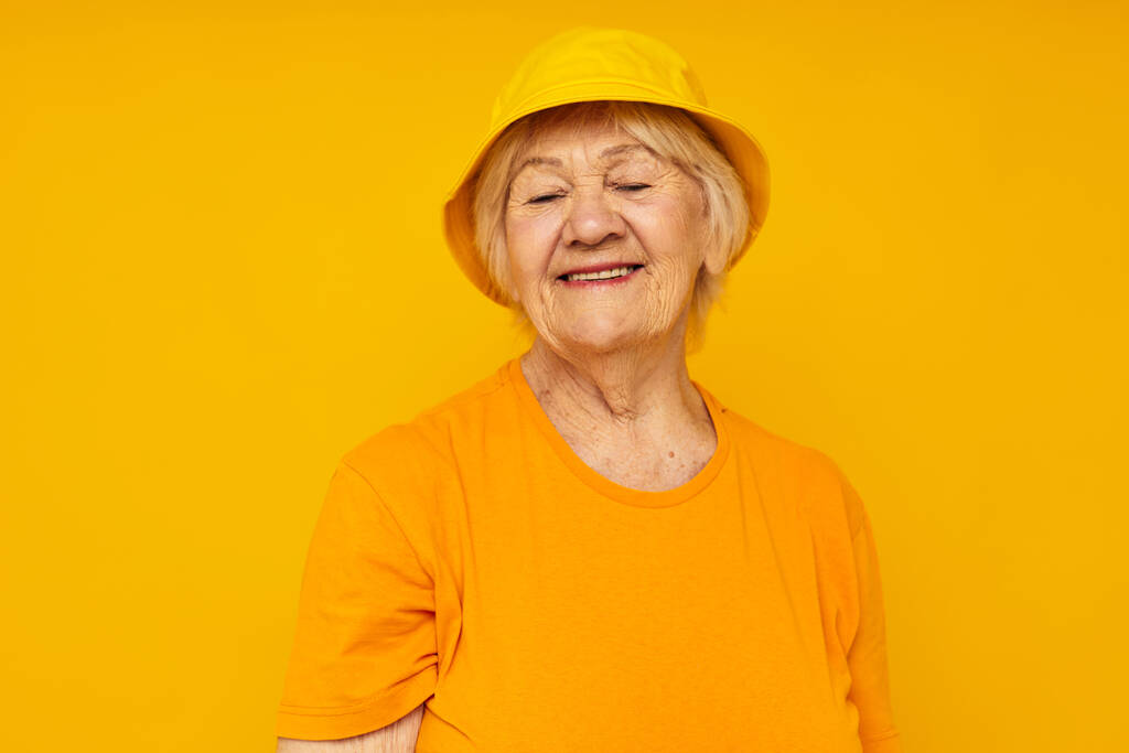 glimlachende oudere vrouw gelukkig levensstijl in een gele hoofdtooi gele achtergrond - Foto, afbeelding