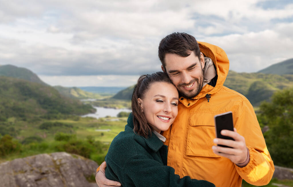 pareja tomando selfie en teléfono sobre irlandés paisaje - Foto, Imagen