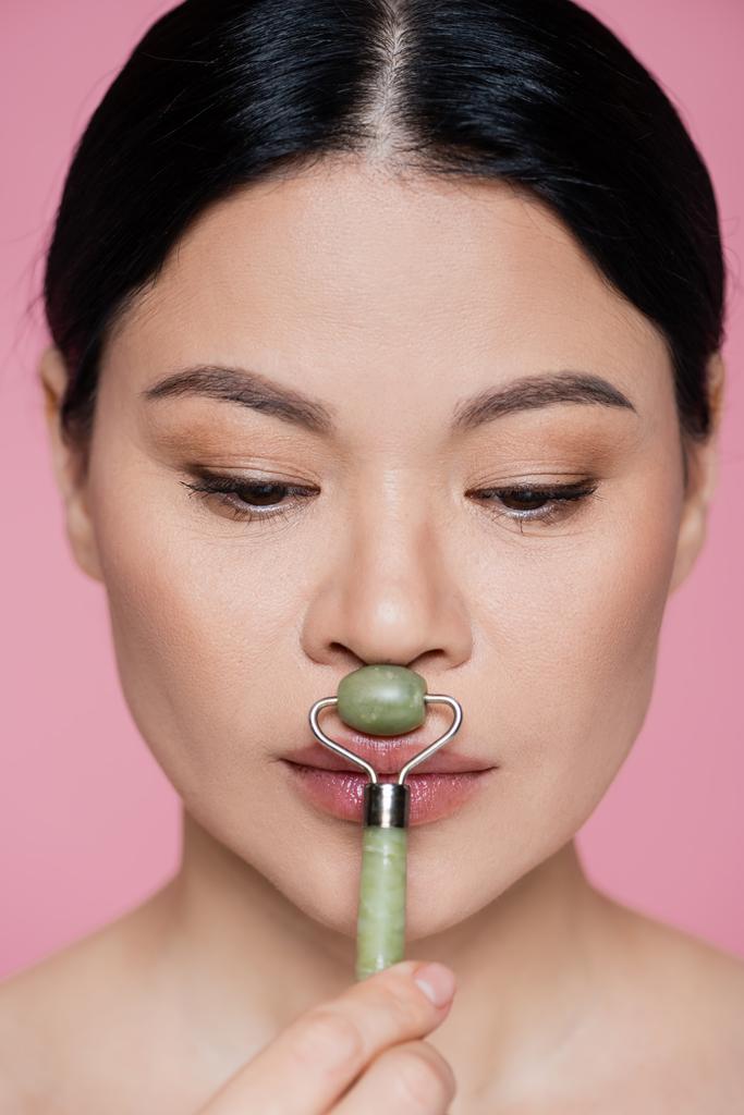 Mulher asiática massageando rosto com jade rolo isolado em rosa  - Foto, Imagem