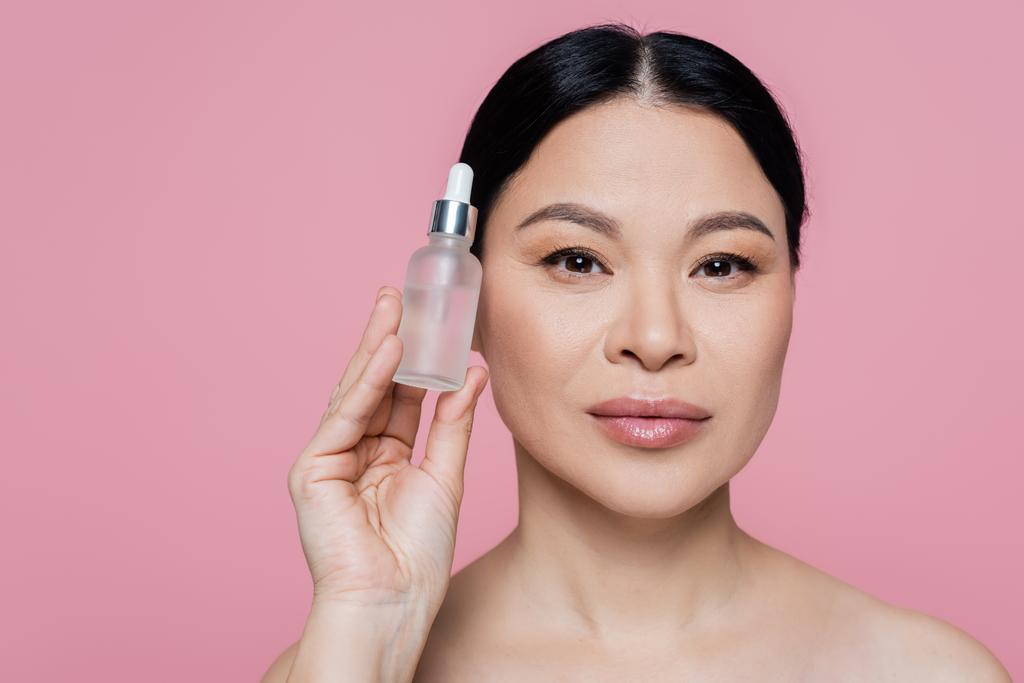 Donna asiatica bottiglia con siero cosmetico isolato su rosa  - Foto, immagini