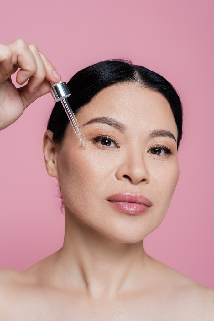 Asian woman applying serum on face isolated on pink  - Photo, Image