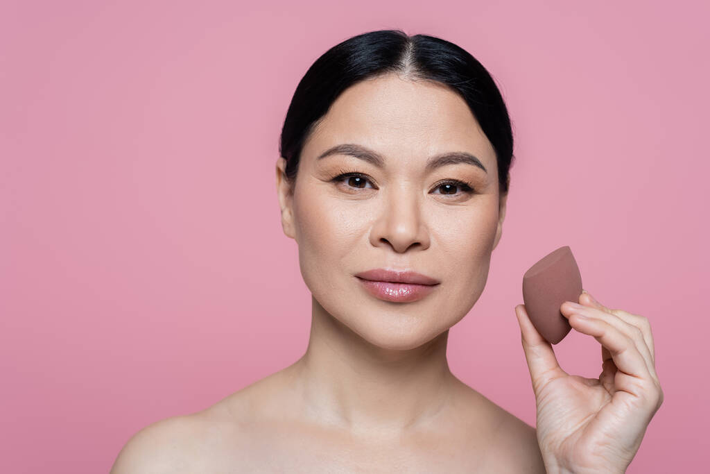 Asian woman with naked shoulders holding beauty blender isolated on pink  - Photo, Image