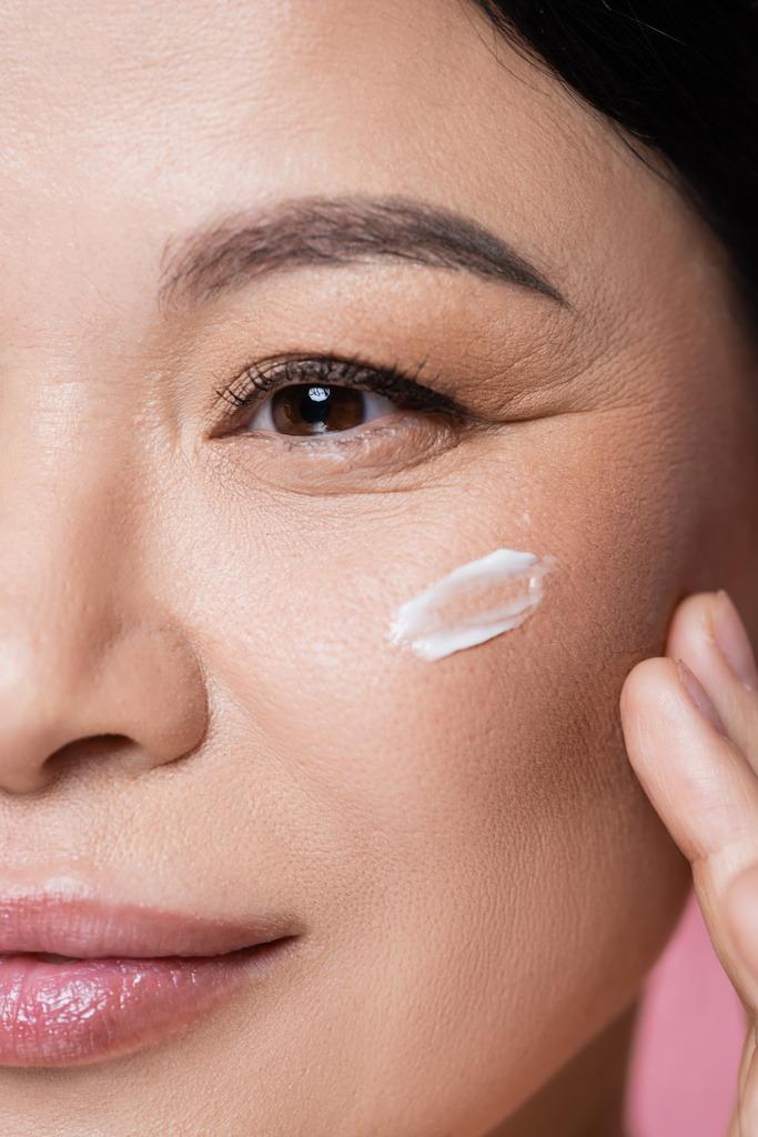 Close up view of asian woman applying face cream isolated on pink  - Photo, Image