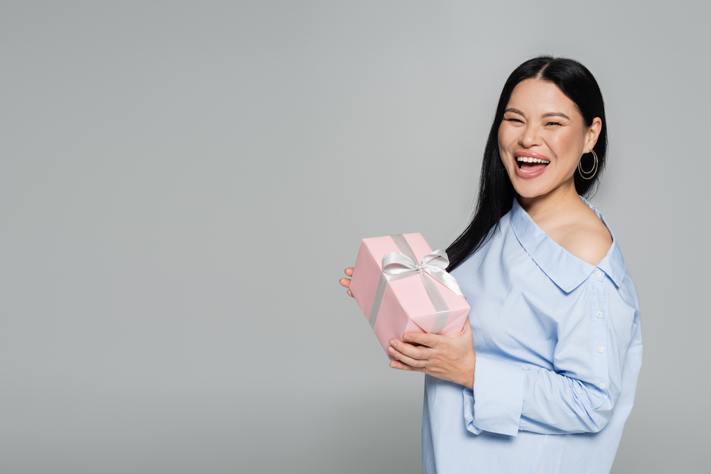 Joyful asian woman holding present isolated on grey  - Photo, Image