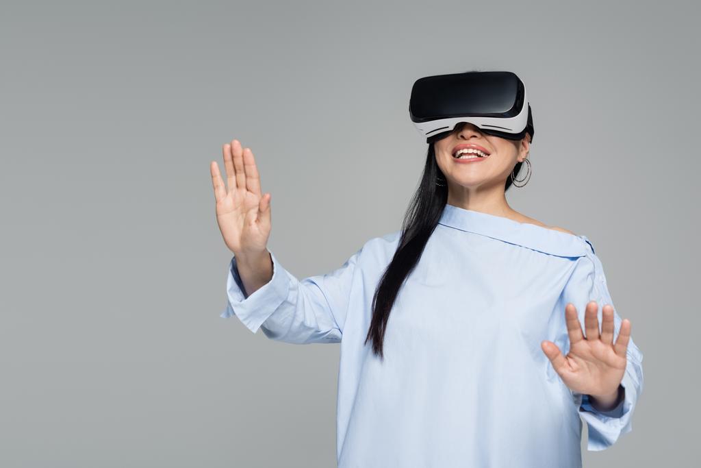 Веселая женщина игры в VR гарнитуры изолированы на серый  - Фото, изображение