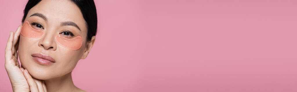 model azjatycki z przepaskami na oczy patrząc na aparat odizolowany na różowy, baner  - Zdjęcie, obraz