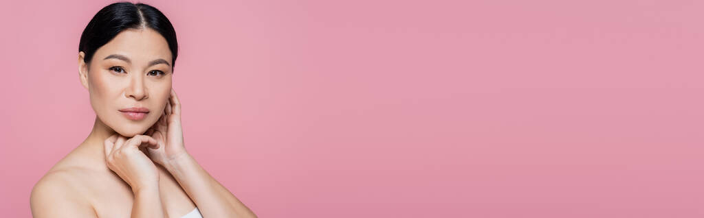Mujer asiática con hombro desnudo mirando a la cámara aislada en rosa con espacio de copia, pancarta  - Foto, imagen