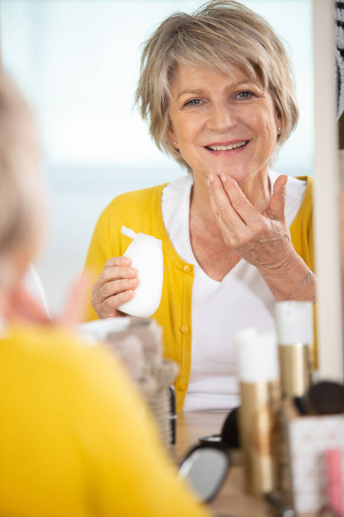 sorrindo mulher sênior aplicando loção anti-envelhecimento - Foto, Imagem