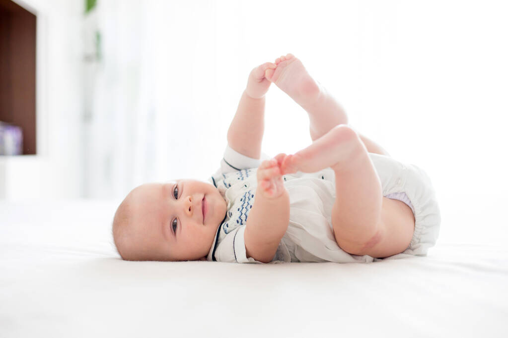 Cute little four month old baby boy, playing at home in bed in bedroom, soft back light behind him - Photo, Image