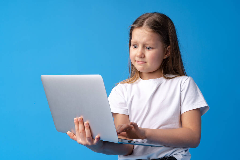 Mavi arka planda dizüstü bilgisayar tutan küçük bir kızın portresi - Fotoğraf, Görsel
