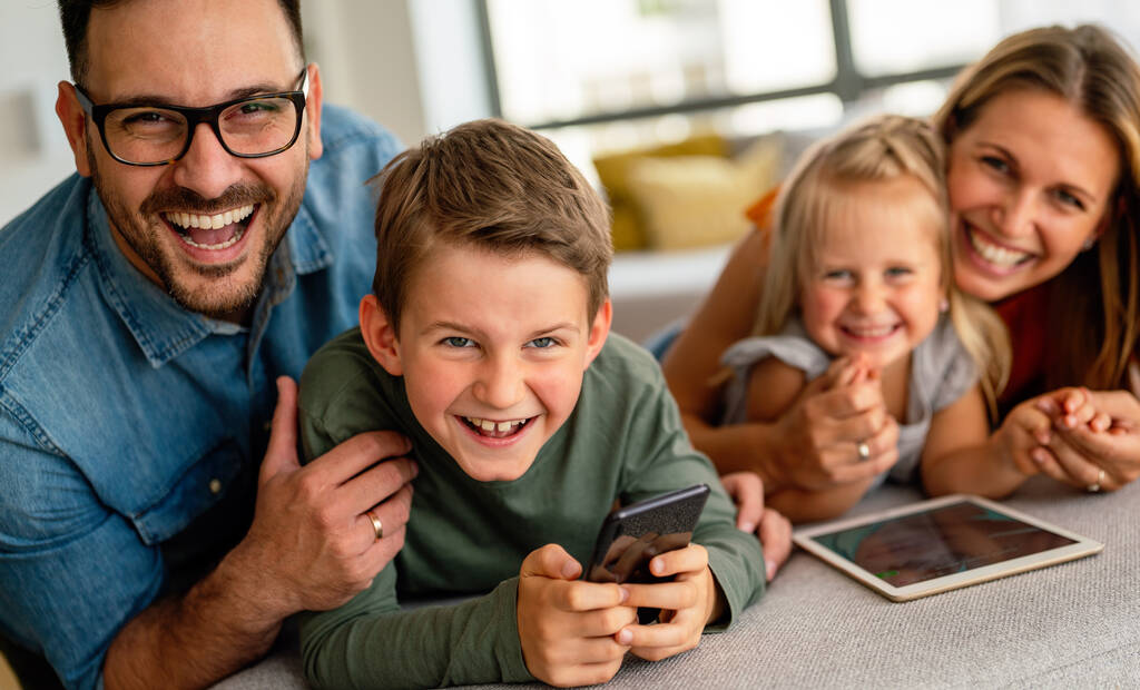 Boldog fiatal család, jól érzik magukat otthon. Digitális eszközt használó gyermekes szülők. Oktatás szülői boldogság koncepció. - Fotó, kép