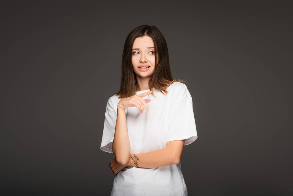 frightened woman in white t-shirt pointing with finger isolated on dark grey - Photo, Image