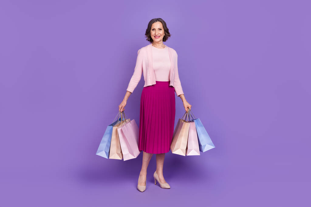 Volledige lengte portret van vrolijke mooie persoon houden pakketten goed humeur geïsoleerd op paarse kleur achtergrond - Foto, afbeelding