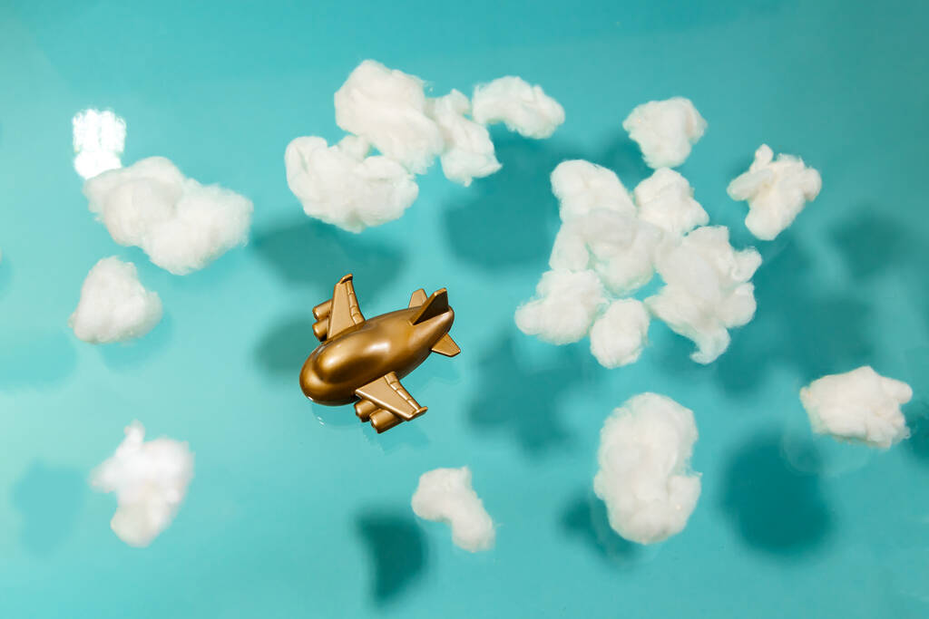 Zabawkowy samolot lata wśród białych bawełnianych chmur na pastelowym niebieskim tle. Koncepcja podróży. - Zdjęcie, obraz