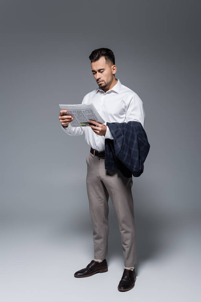 Vollbärtiger Geschäftsmann im Anzug liest Zeitung auf grau - Foto, Bild