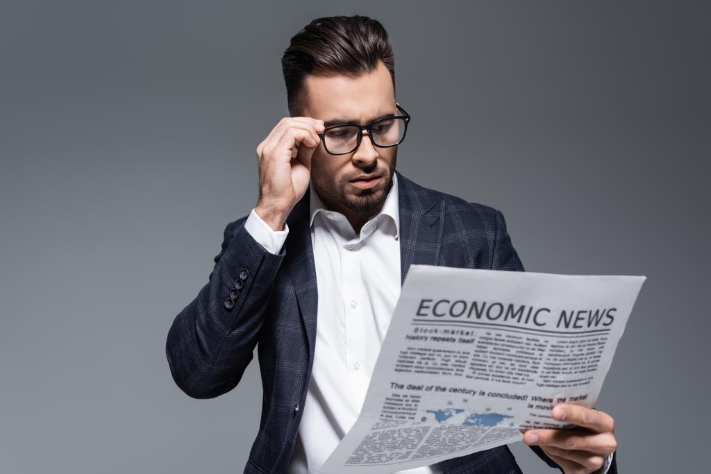 szakállas üzletember kockás blézerben és szemüvegben újságot olvas, gazdasági hírekkel elszigetelve a szürkén. - Fotó, kép