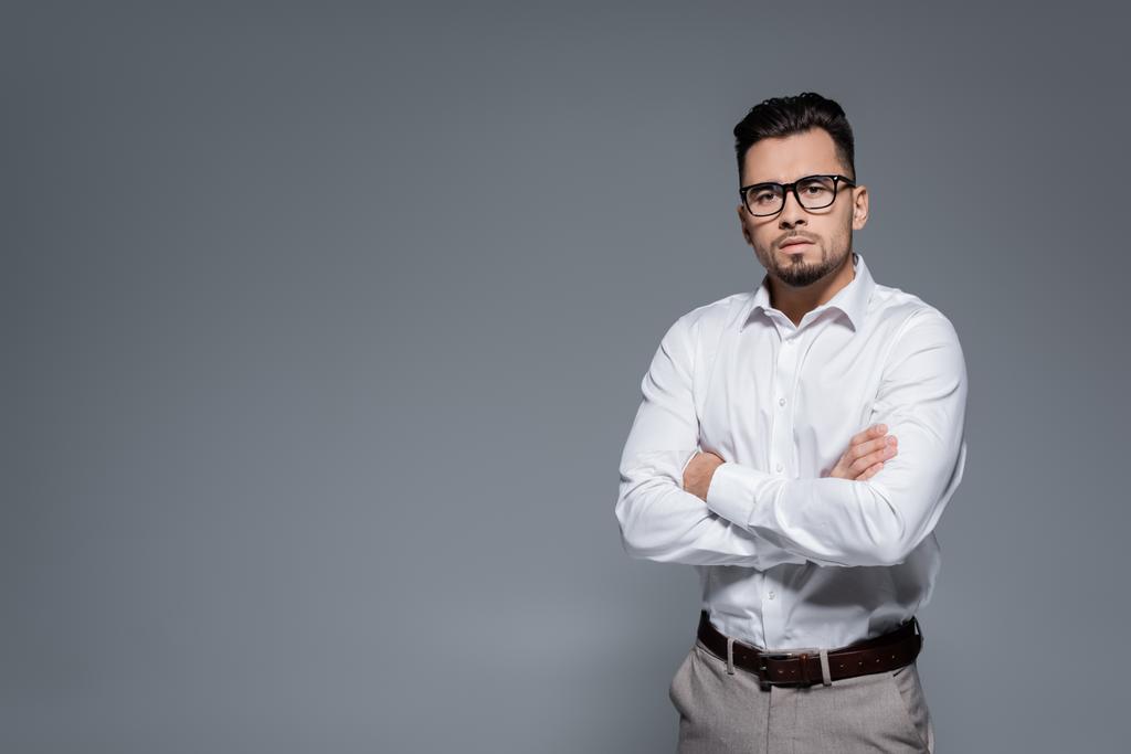 γενειοφόρος επιχειρηματίας σε λευκό πουκάμισο και γυαλιά στέκεται με σταυρωμένα χέρια απομονώνονται σε γκρι - Φωτογραφία, εικόνα