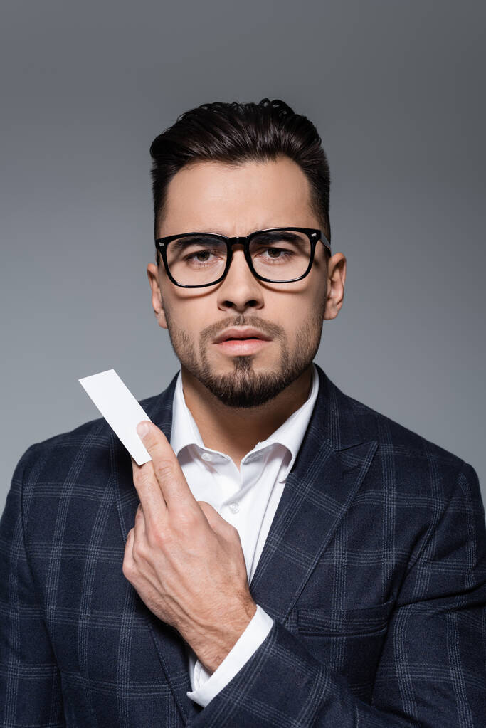 obchodník v brýlích a obleku drží prázdnou kartu izolovanou na šedé - Fotografie, Obrázek
