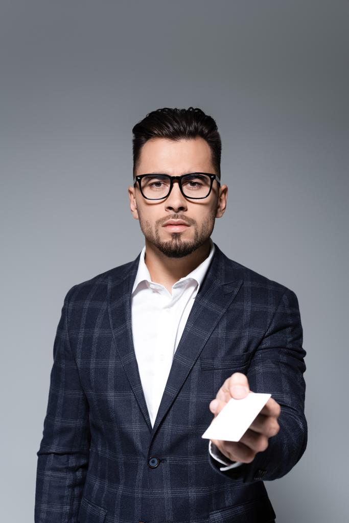 uomo d'affari in occhiali e blazer che offre carta bianca isolata su grigio - Foto, immagini