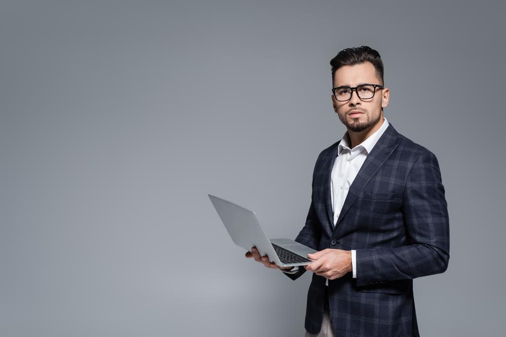 Geschäftsmann in Anzug und Brille hält Laptop isoliert auf grau - Foto, Bild