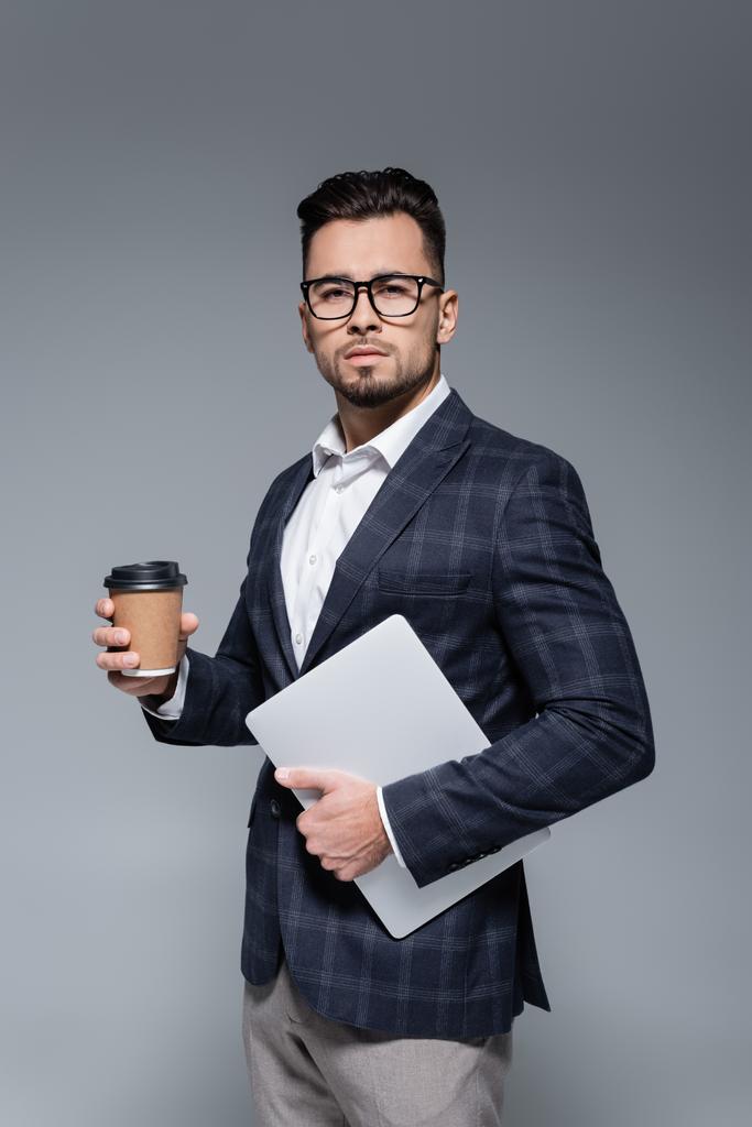 Geschäftsmann in Anzug und Brille hält Laptop und Pappbecher isoliert auf grau - Foto, Bild
