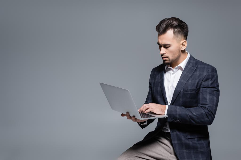 homme d'affaires barbu en costume en utilisant un ordinateur portable isolé sur gris - Photo, image